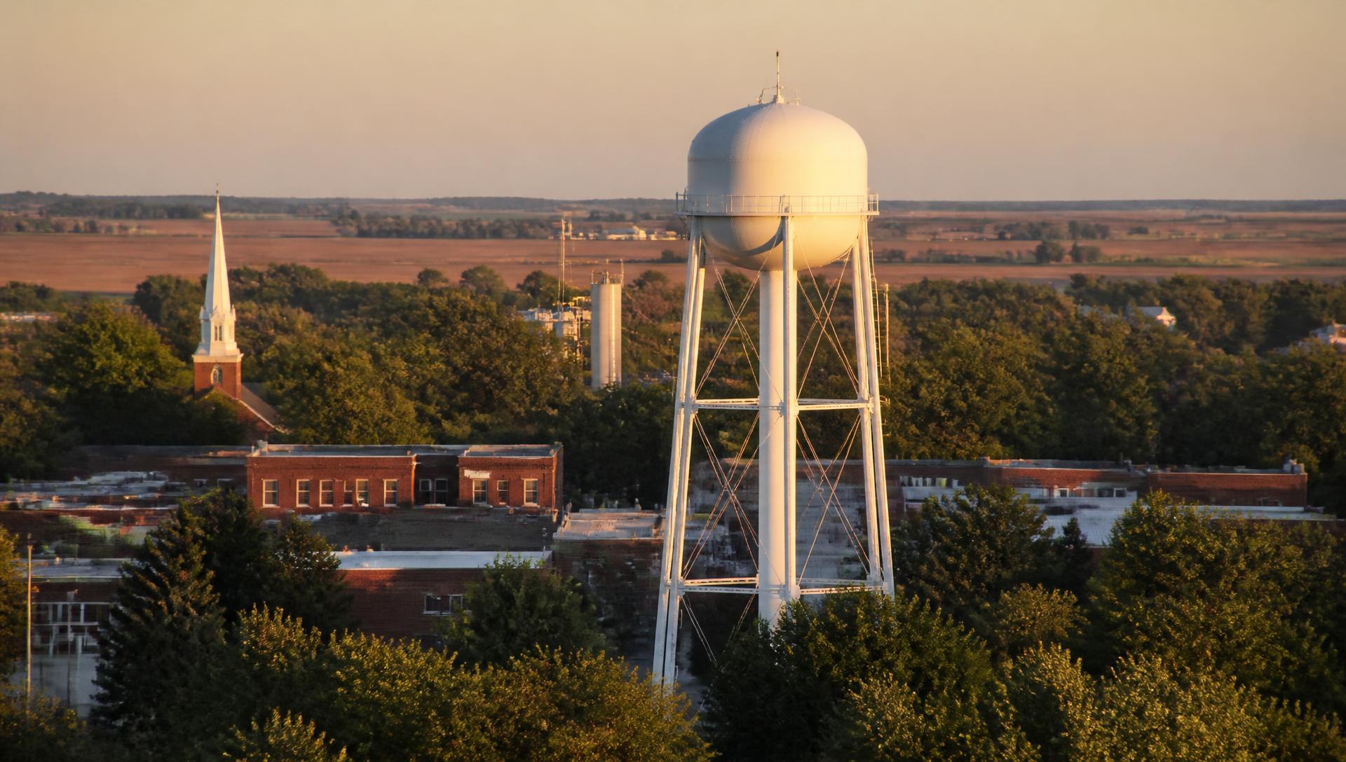 The Arcanum water tower rising above downtown rooftops and surrounding farmland at sunset.